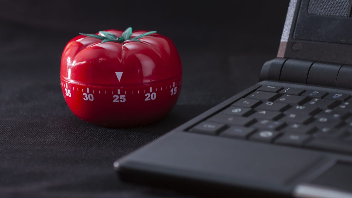 Timer mekanis berbentuk tomat di sebelah laptop PC.