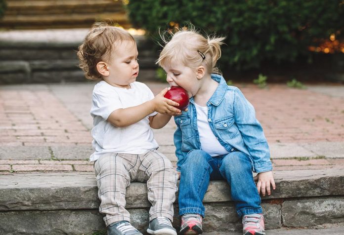Seorang anak kecil berbagi apel dengan seorang gadis kecil