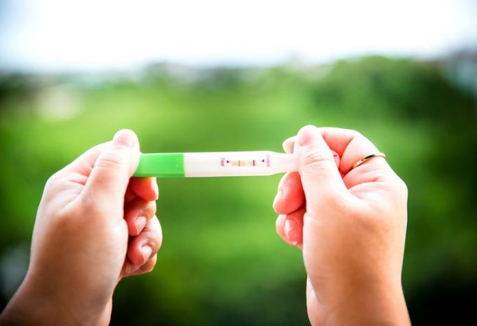 Seorang wanita memegang tes kehamilan positif