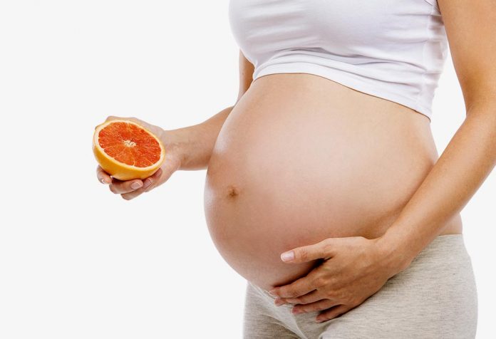 Seorang wanita hamil memegang jeruk di dekat perutnya