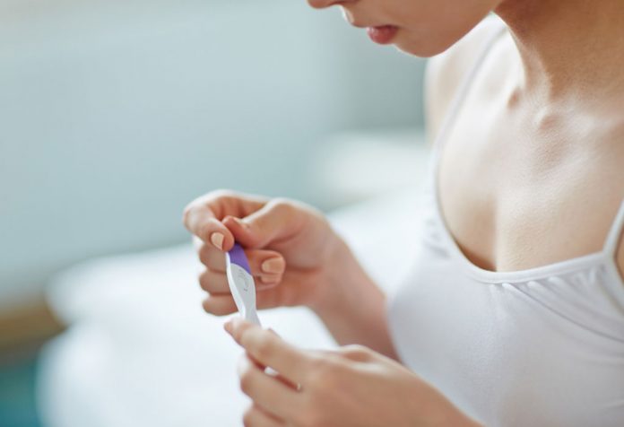Seorang wanita muda dengan alat tes kehamilan di tangannya