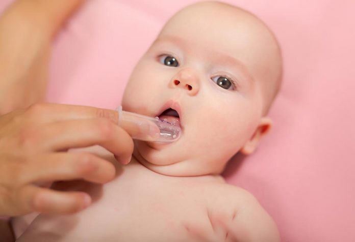 ibu membersihkan gigi bayinya dengan sikat jari silikon