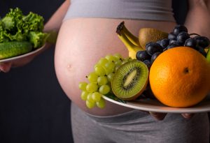 Seorang wanita hamil memegang sepiring buah-buahan