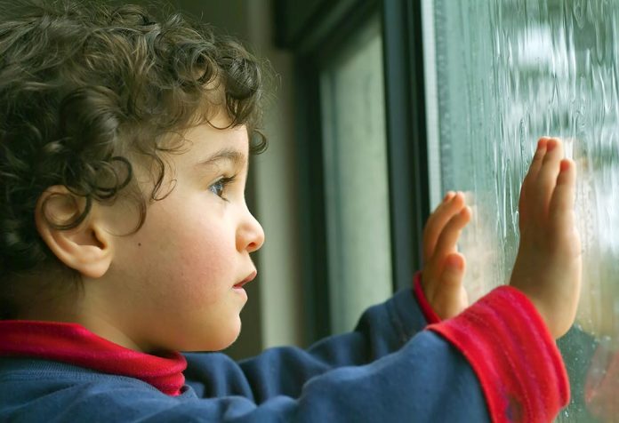 Seorang anak melihat hujan melalui jendela