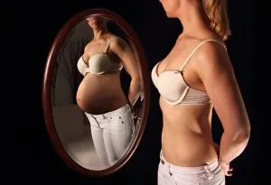 Seorang wanita melihat ke cermin dan membayangkan dirinya hamil