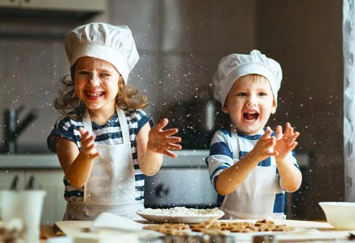 Seorang gadis kecil dan seorang anak laki-laki bermain dengan adonan kue di dapur