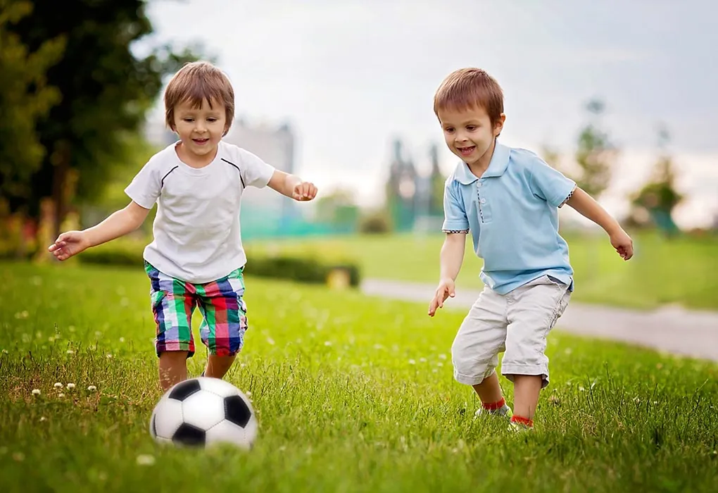 Dua anak laki-laki bermain sepak bola di taman