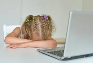 Gadis kecil mengistirahatkan kepalanya di atas meja di depan laptop